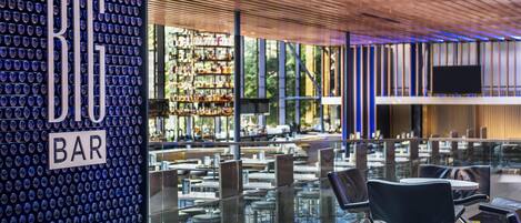 A modern bar with a unique glass wall design, a wooden ceiling, and a view of the outdoor seating area.