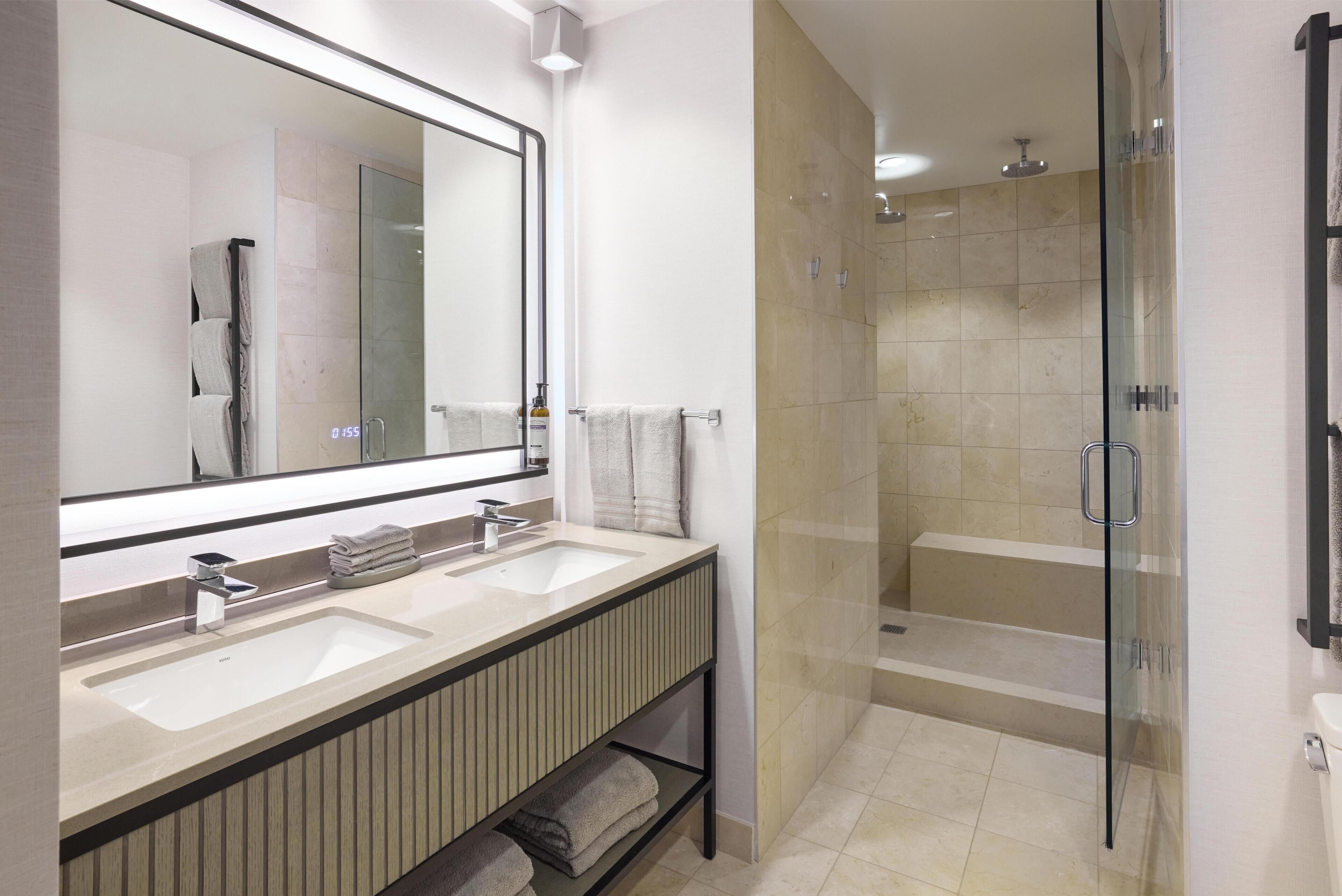 Un baño moderno con dos lavamanos, un espejo grande y una ducha con cerramiento de vidrio.