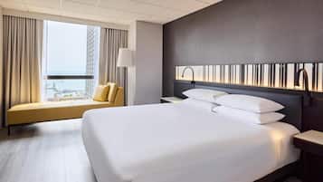 A hotel room with a large bed, a sofa, a nightstand, a lamp, and a view of the city.