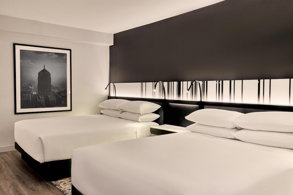 A hotel room with two beds, a large framed cityscape picture, and a modern headboard.