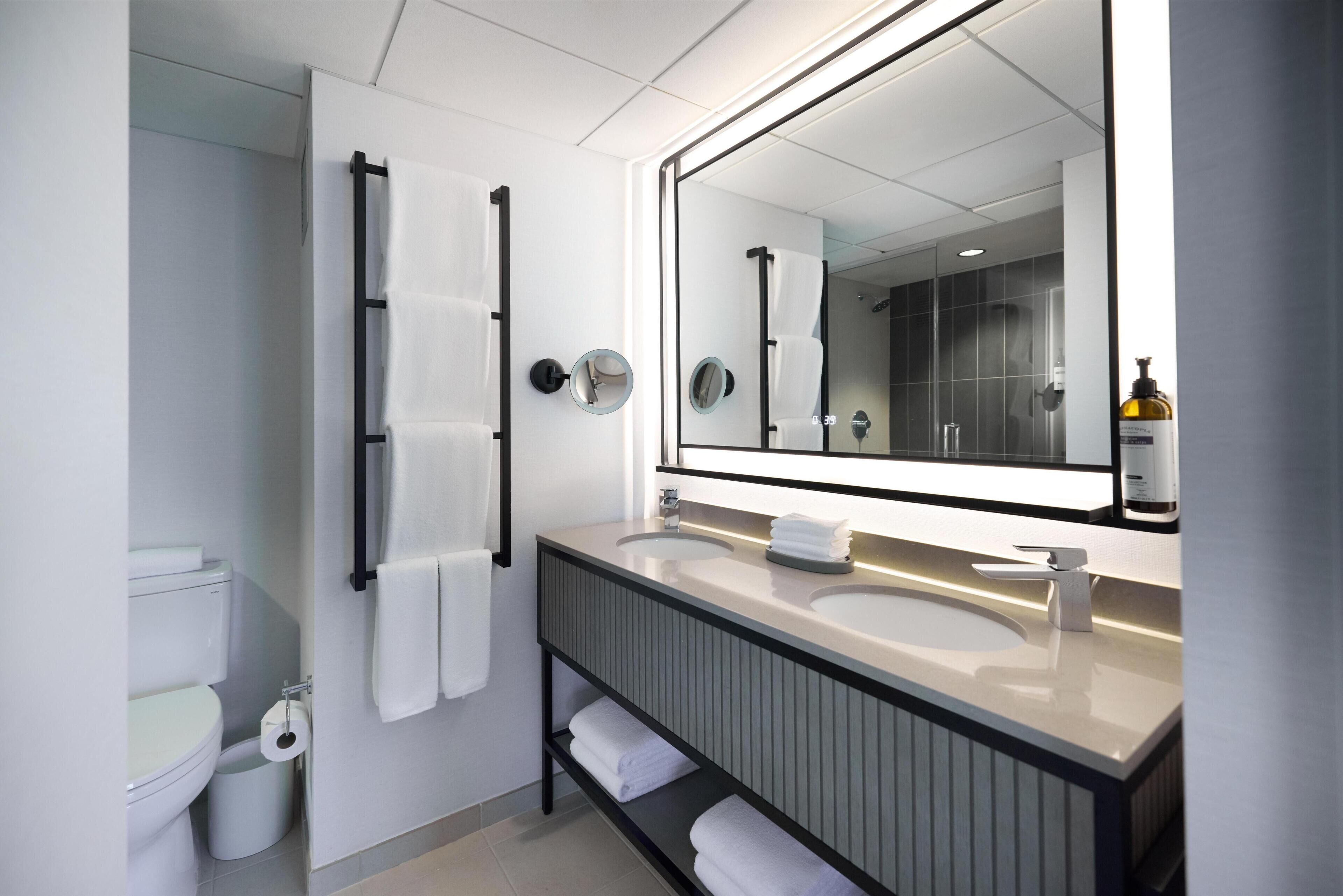 Un baño moderno con un espejo grande, dos lavamanos, un inodoro y un perchero para toallas.