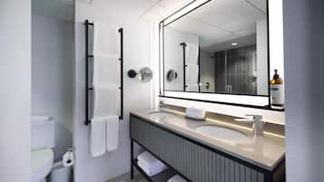 A modern bathroom with a large mirror, two sinks, a toilet, and a towel rack.