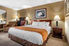 A hotel room with a large bed, two bedside lamps, a chair, a desk with a telephone, and a framed picture on the wall.