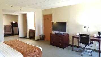 A hotel room with a bed, a desk with a computer, a chair, a TV, a microwave, and a small refrigerator.