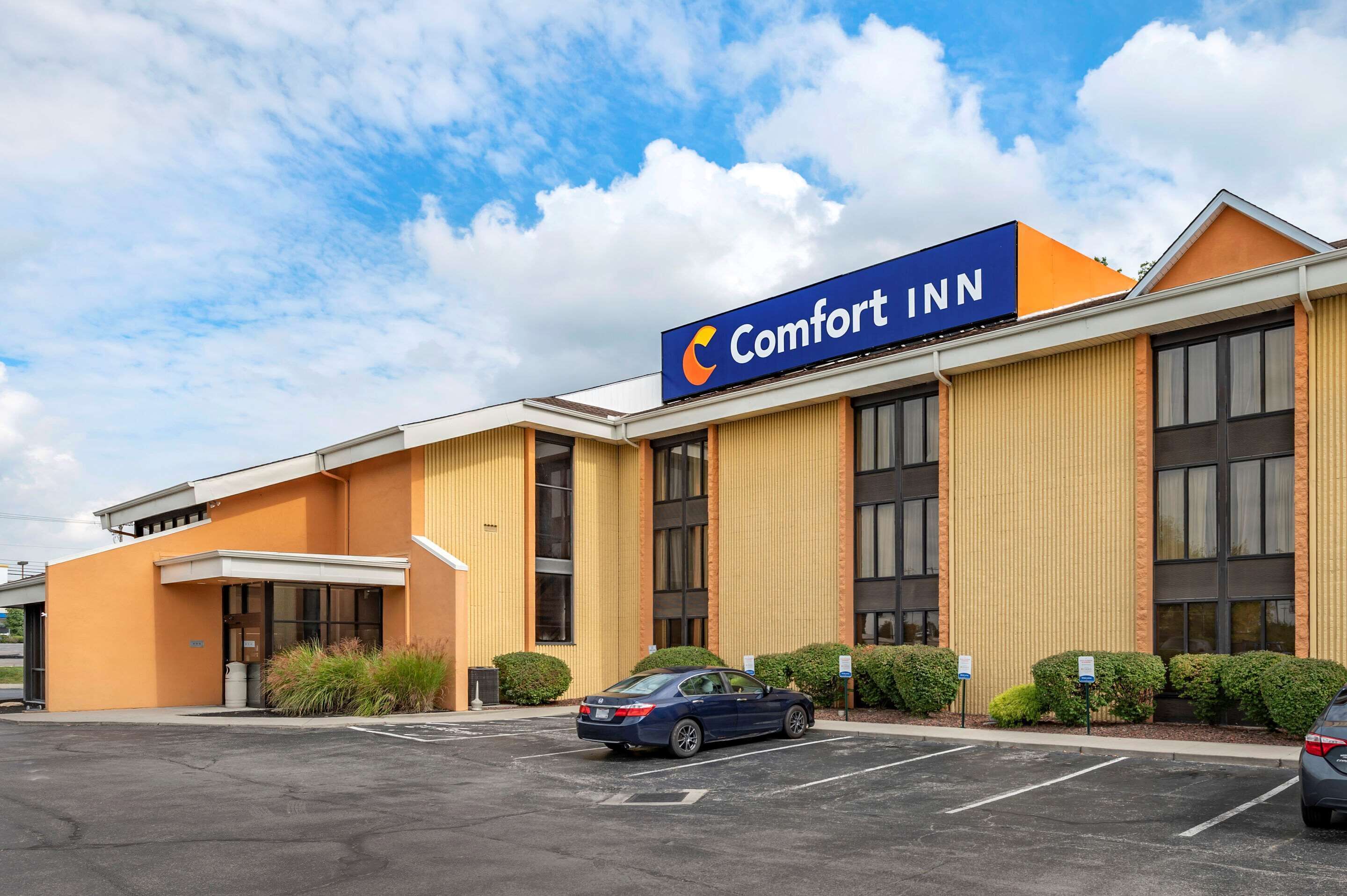 A Comfort Inn hotel with a large sign, a parking lot, and a blue car parked in front.