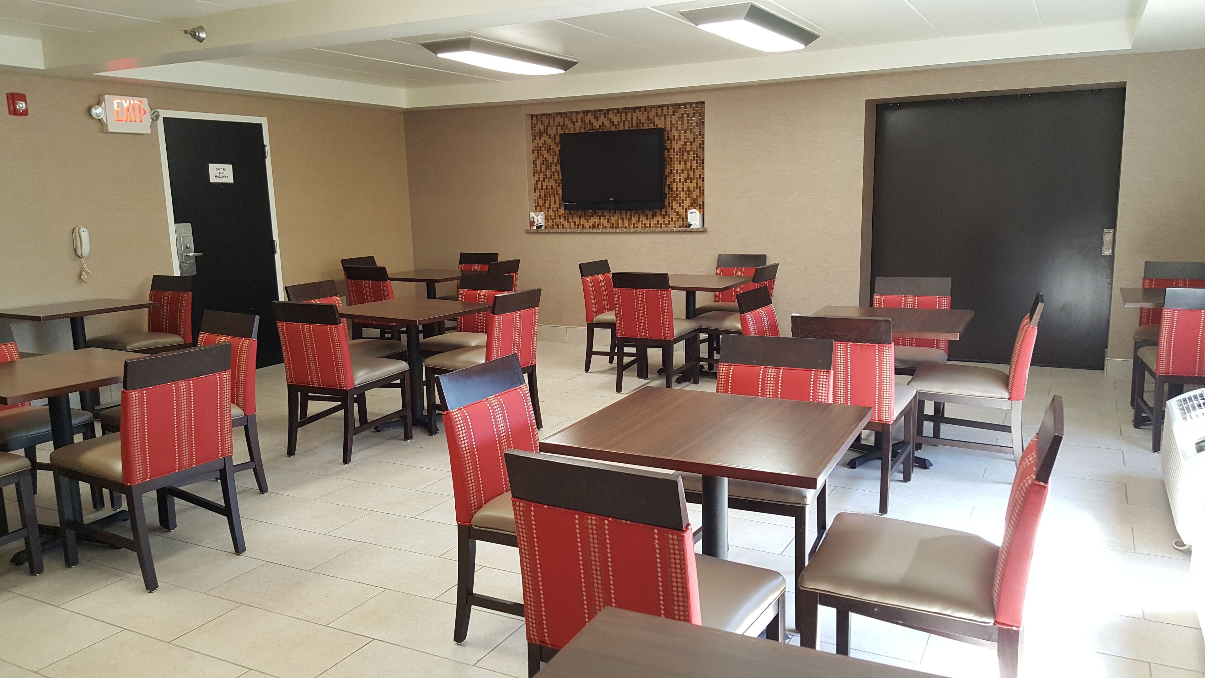 A conference room with tables and chairs, a television on the wall, and an exit sign.