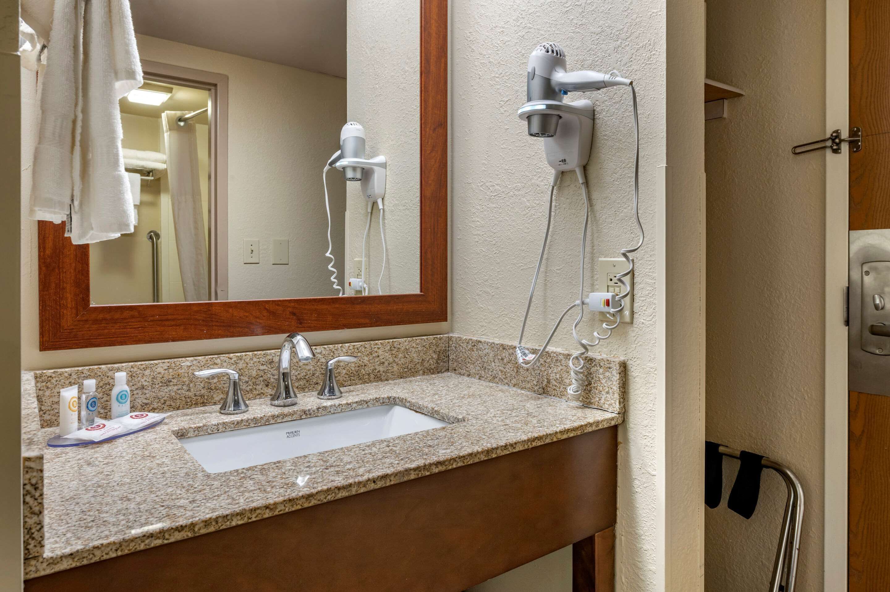 A bathroom with a granite countertop sink, a mirror, a hairdryer, and a shower curtain.