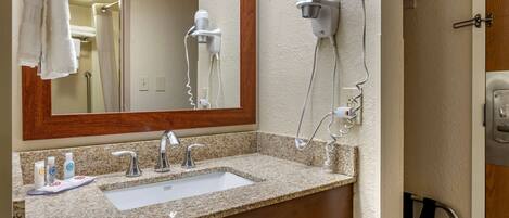 A bathroom with a granite countertop sink, a mirror, a hairdryer, and a shower curtain.