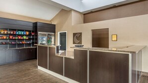 Un área de recepción moderna con mostrador, vitrina refrigerada y estantes para aperitivos.