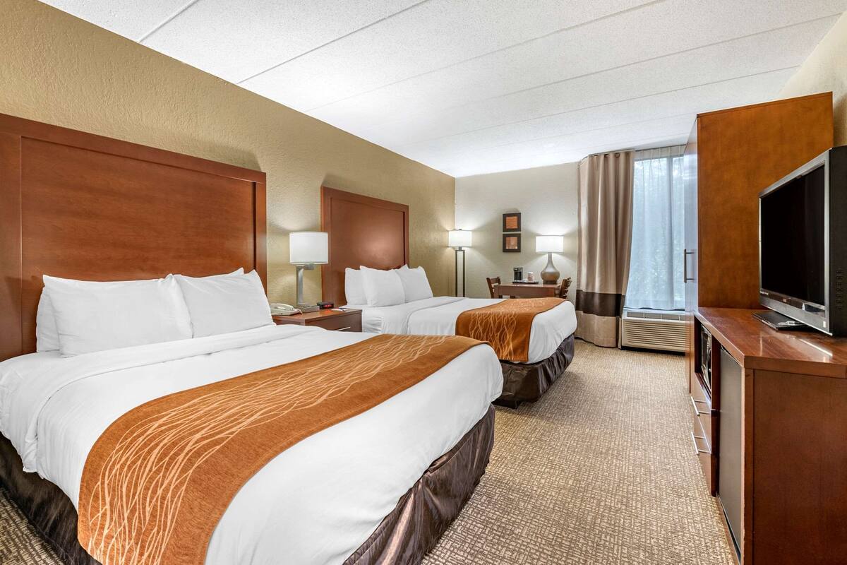 A hotel room with two beds, a TV, a desk, and a window with curtains.