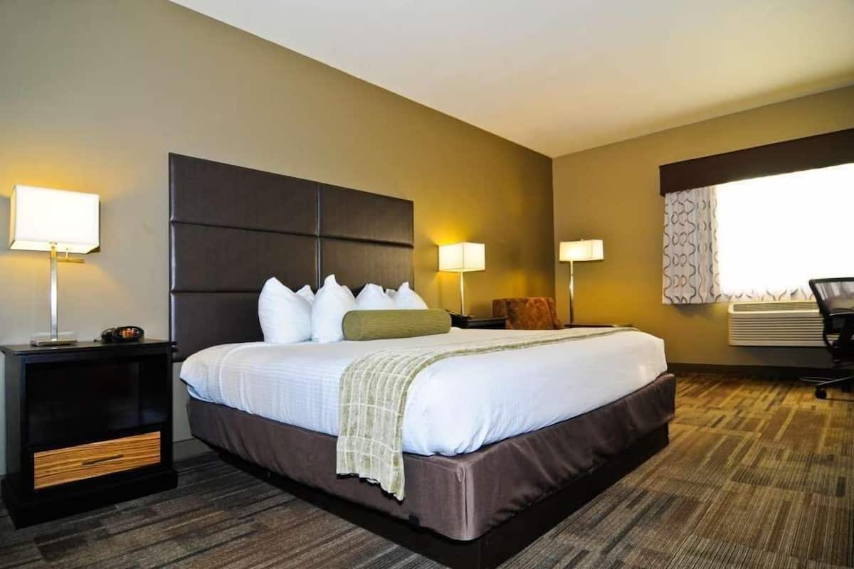 A hotel room with a large bed, two bedside tables with lamps, a chair, and a window with curtains.