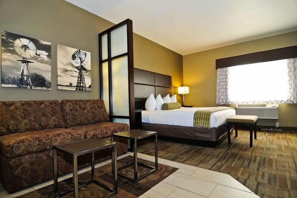 A hotel room with a bed, a sofa, a small table, and two wall-mounted artworks depicting windmills.