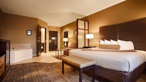 Habitación de hotel con una cama grande, un banco, un escritorio, una silla, un televisor y un baño con bañera e inodoro.