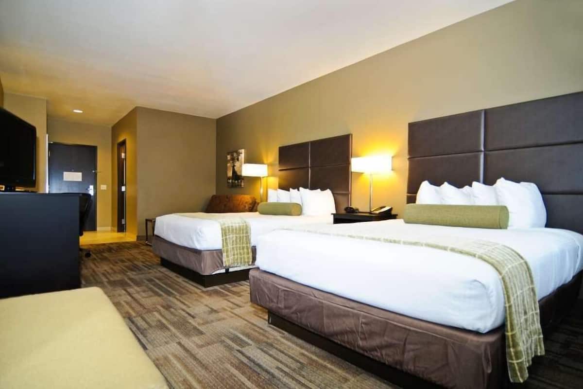 A hotel room with two beds, a desk, and a TV.