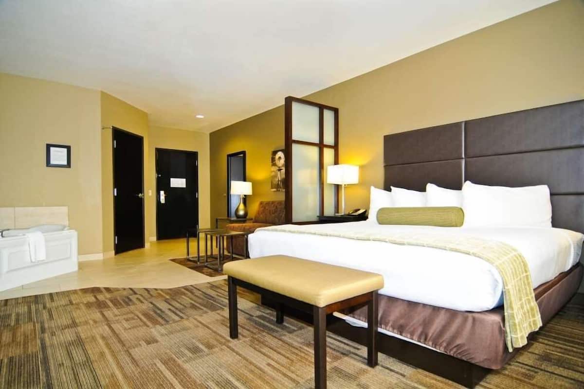 A hotel room with a large bed, a bench, a desk with a lamp, and a sofa.