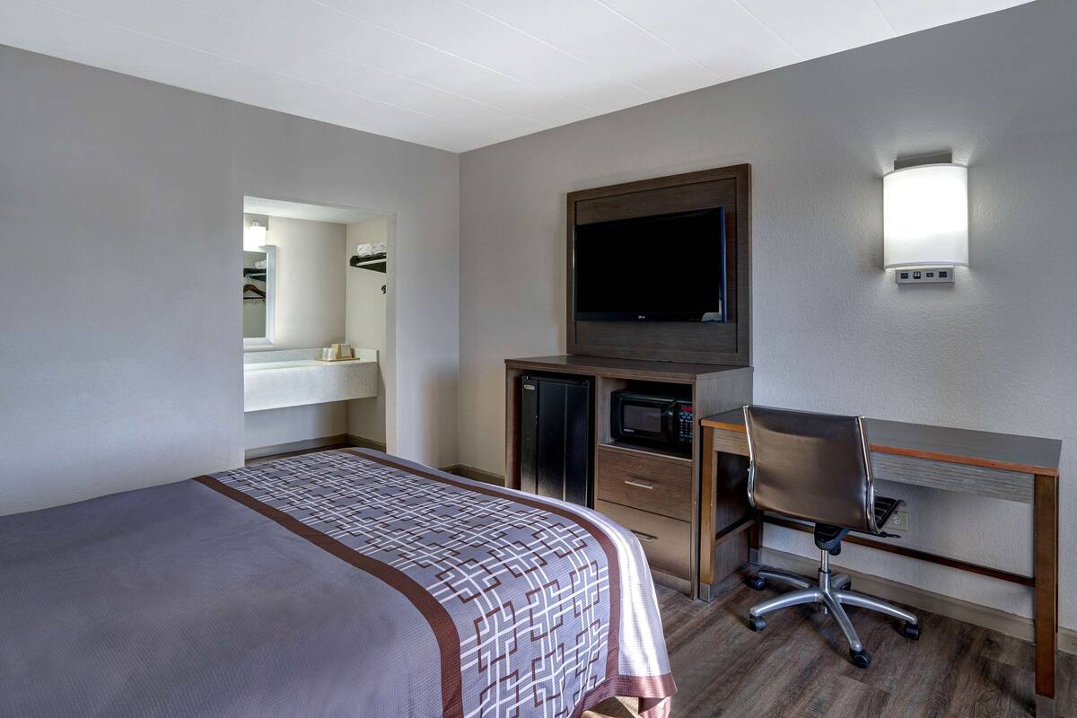 Habitación de hotel con cama, escritorio con silla, televisor, microondas y espejo.