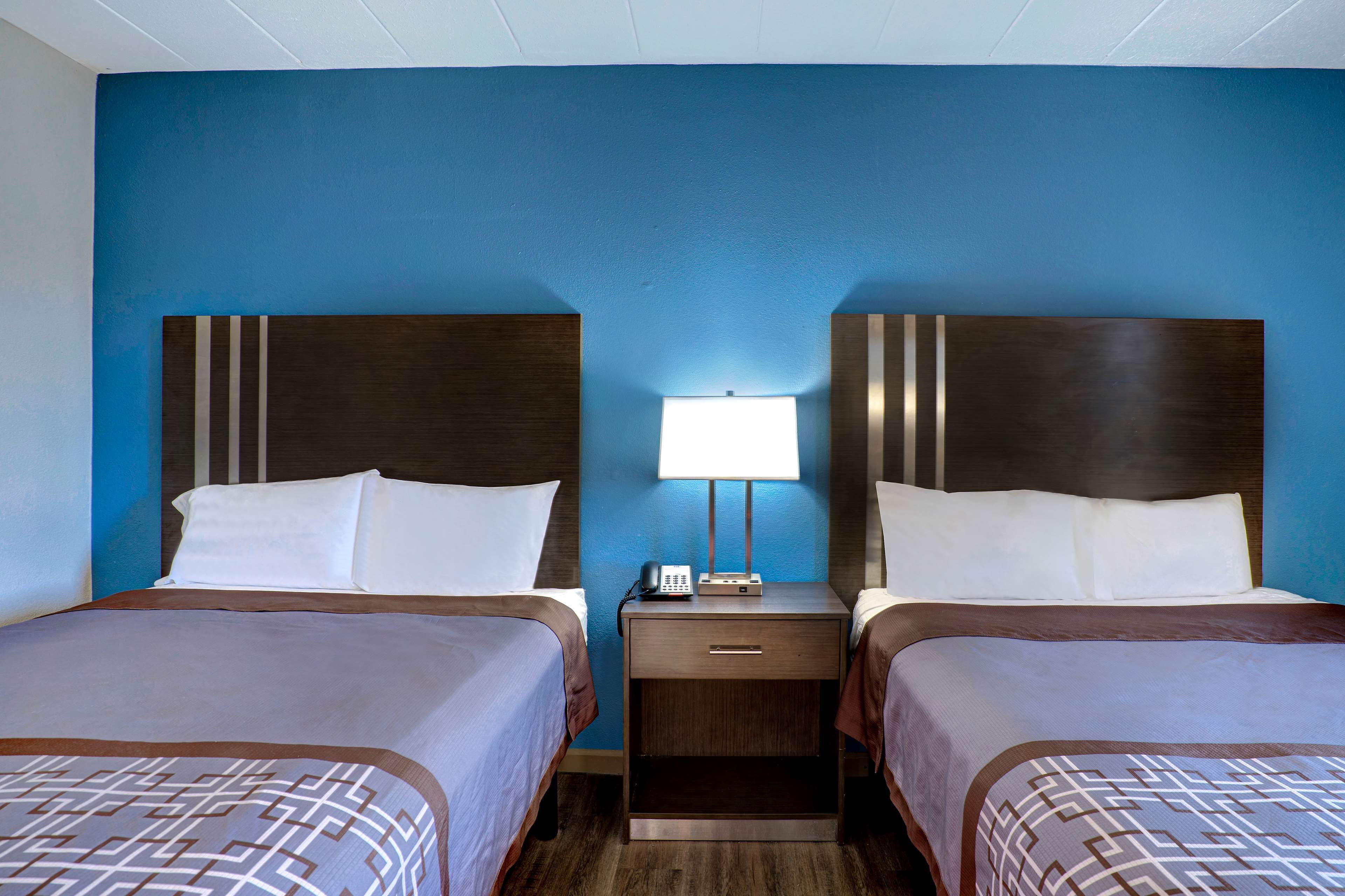 A hotel room with two beds, a nightstand with a lamp, and a blue wall.