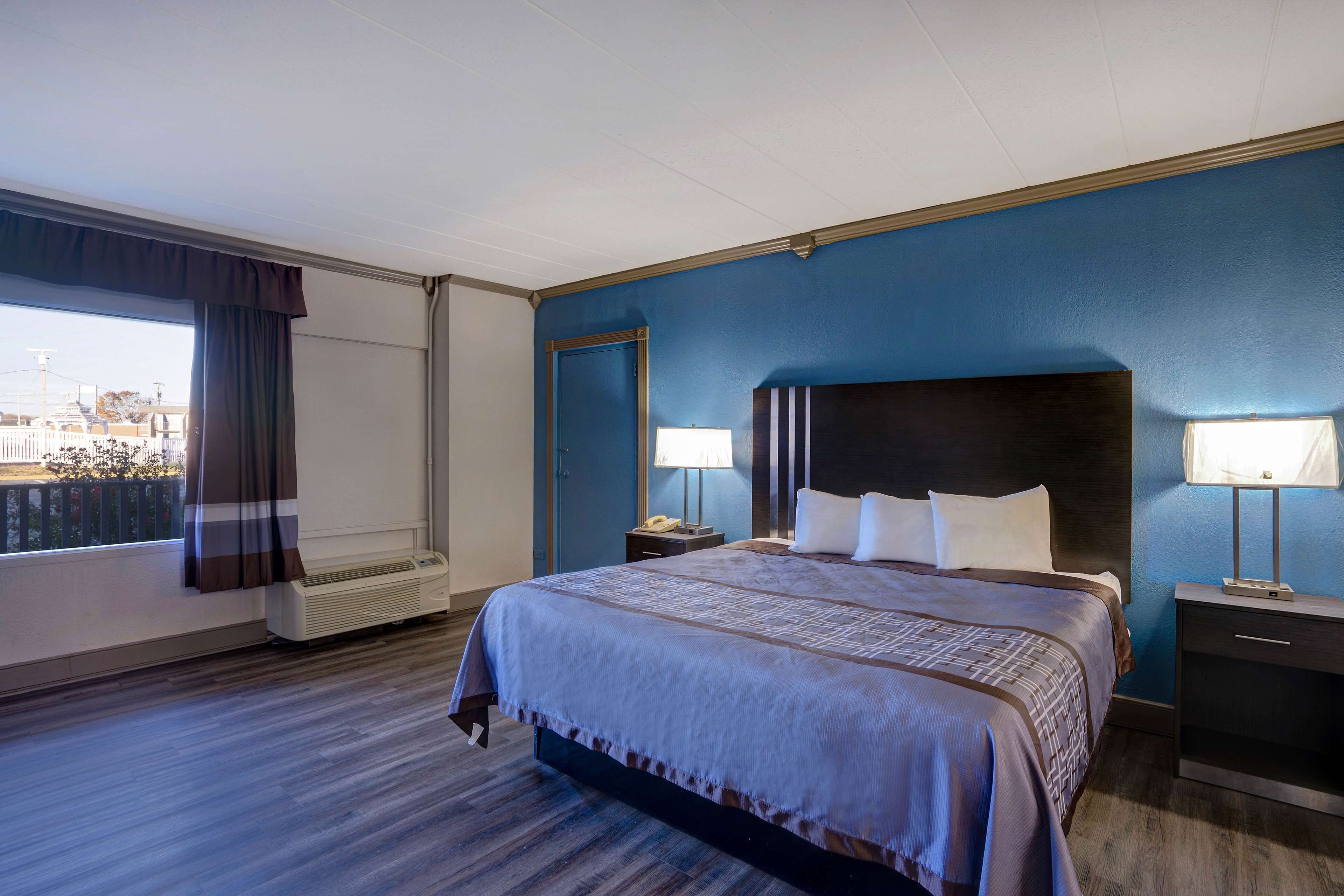 Une chambre d’hôtel avec un grand lit, deux tables de chevet avec des lampes, une fenêtre avec des rideaux et une vue sur les bâtiments environnants.