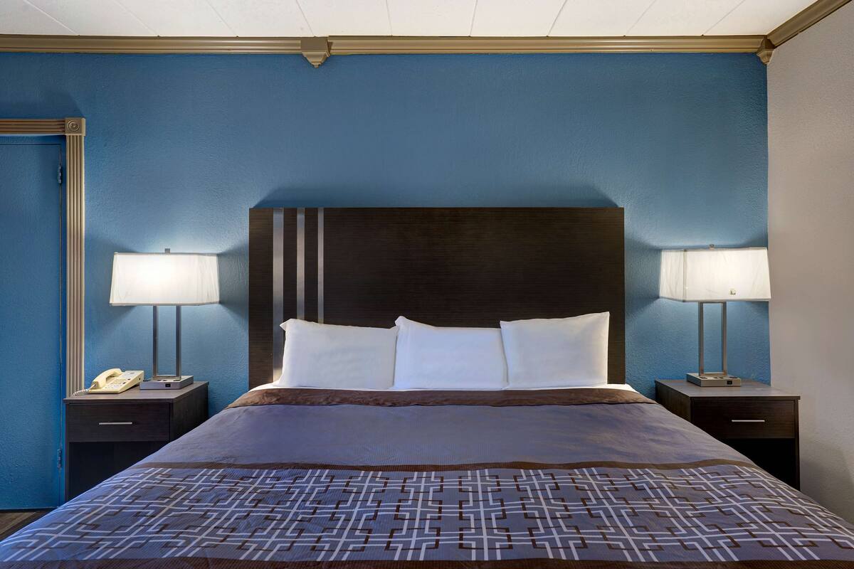 Una habitación de hotel con una cama grande, dos mesitas de noche, un teléfono y dos lámparas.