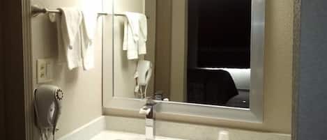 A hotel bathroom with a sink, a mirror, a hairdryer, and a towel rack.