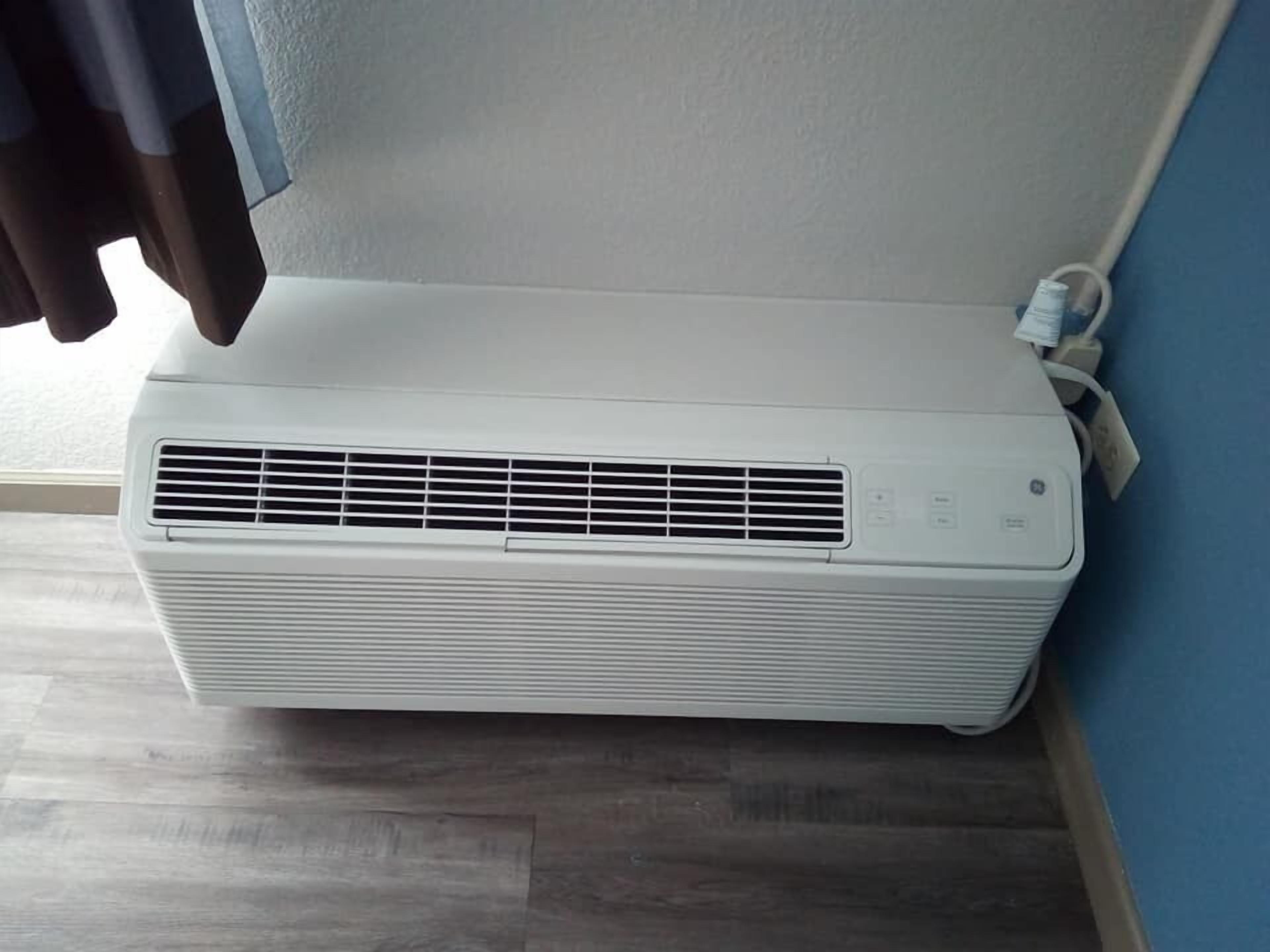 A white portable air conditioner in a corner with a window and a blue wall.