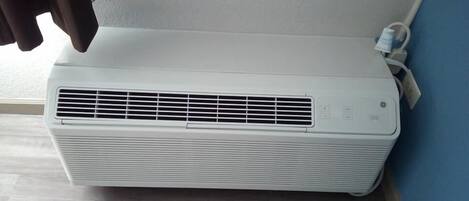A white portable air conditioner in a corner with a window and a blue wall.