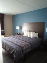 Una habitación de hotel con una cama grande, cabecero, mesita de noche con lámpara y ventana con cortinas.