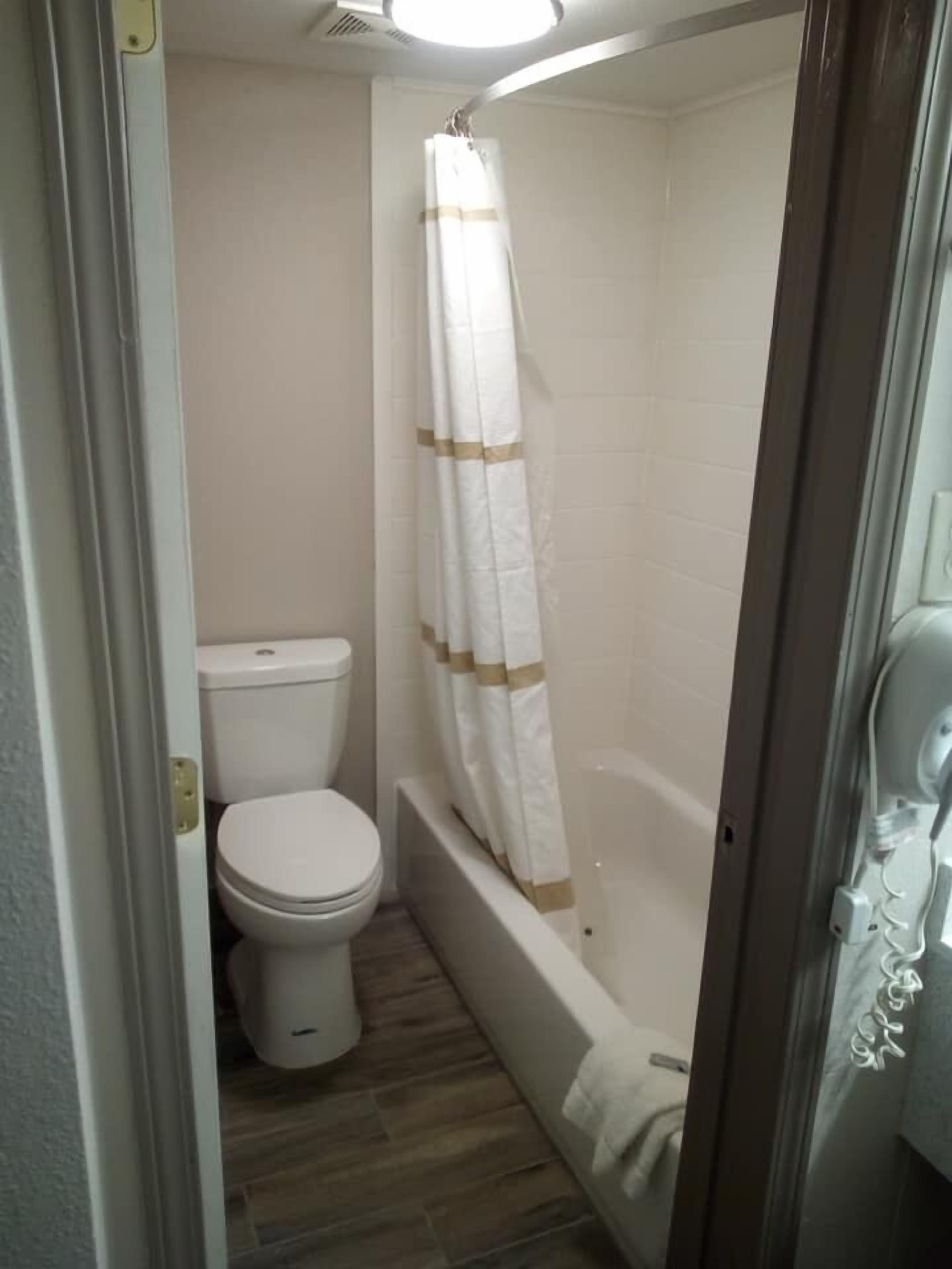A small bathroom with a toilet, a shower with a curtain, and a bathtub.