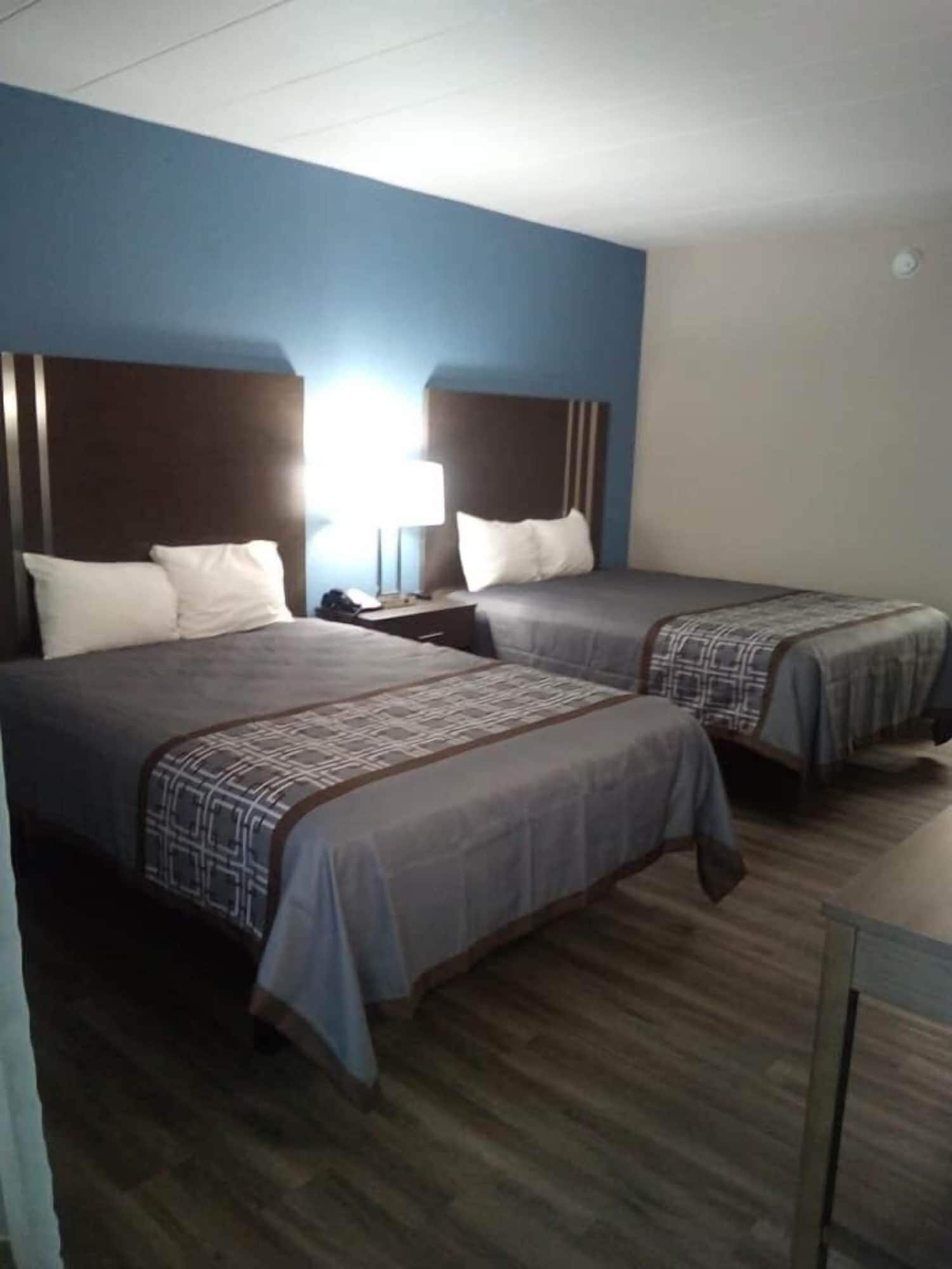 A hotel room with two beds, a nightstand, and a desk.