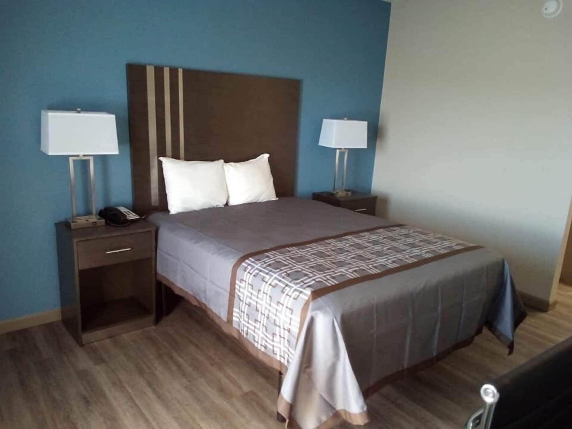 Quarto de hotel com uma cama, duas mesas de cabeceira com luminárias, um telefone e piso de madeira.