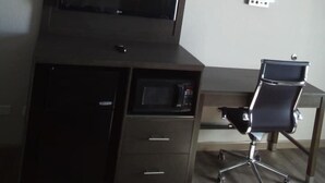 A room with a dark wooden desk, a black office chair, a flat-screen TV, and a white air conditioning unit on the wall. - Motel 6 Burlington, NC (Burlington)