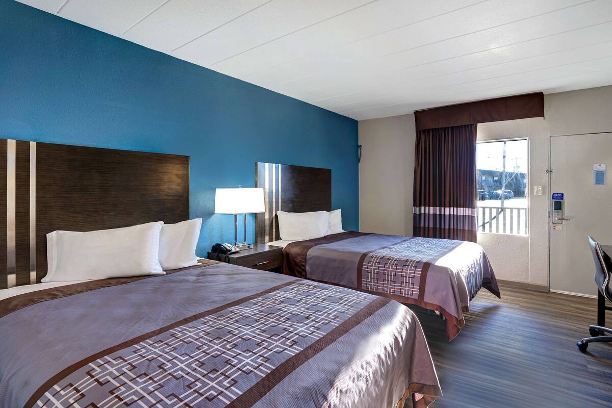 Habitación de hotel con dos camas, un escritorio con silla, una ventana con cortinas y una puerta con cerradura electrónica.