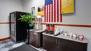 A hotel lobby with a coffee station, a large American flag, and a sign encouraging saving money for travel. - Motel 6 Burlington, NC (Burlington)