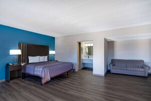 Una habitación de hotel con cama, mesita de noche, lámpara y un sofá.