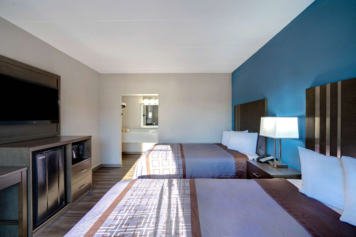 Una habitación de hotel con cama, mesita de noche, lámpara y televisor sobre un mueble.
