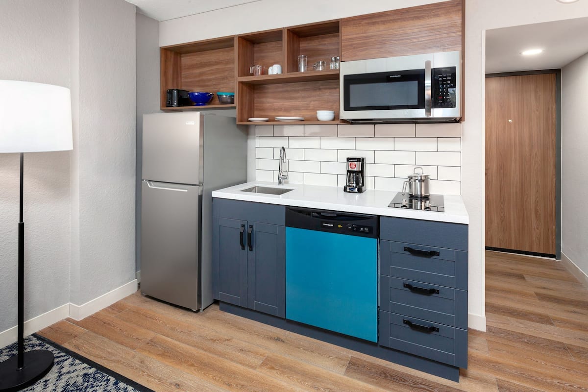 Een moderne keuken met een ingebouwde magnetron, een vaatwasser en houten planken boven het aanrecht.