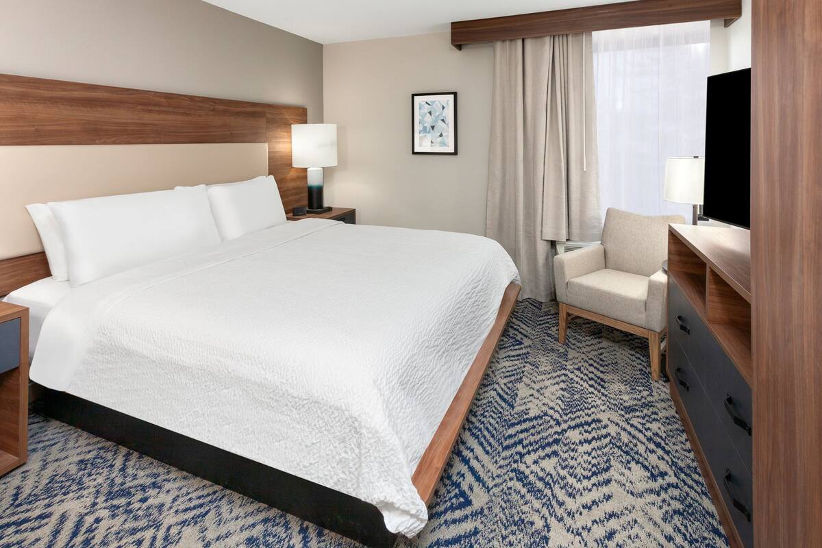 Een hotelkamer met een groot bed, een bureau met stoel, een televisie en een raam met gordijnen.