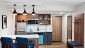 Een moderne keuken met een centraal eiland, een ingebouwde magnetron en een vaatwasser. Er staan twee blauwe stoelen aan een witte tafel, en er is een bankje in de hoek.