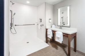 Un baño moderno con ducha a nivel, barras de apoyo, un lavabo con espejo y un perchero para toallas.