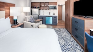 Een hotelkamer met een bed, een bureau met lamp, een stoel, een televisie, een kitchenette met een magnetron en een koffiezetapparaat.