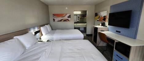 A hotel room with two beds, a desk, a chair, a TV, and a mirror.
