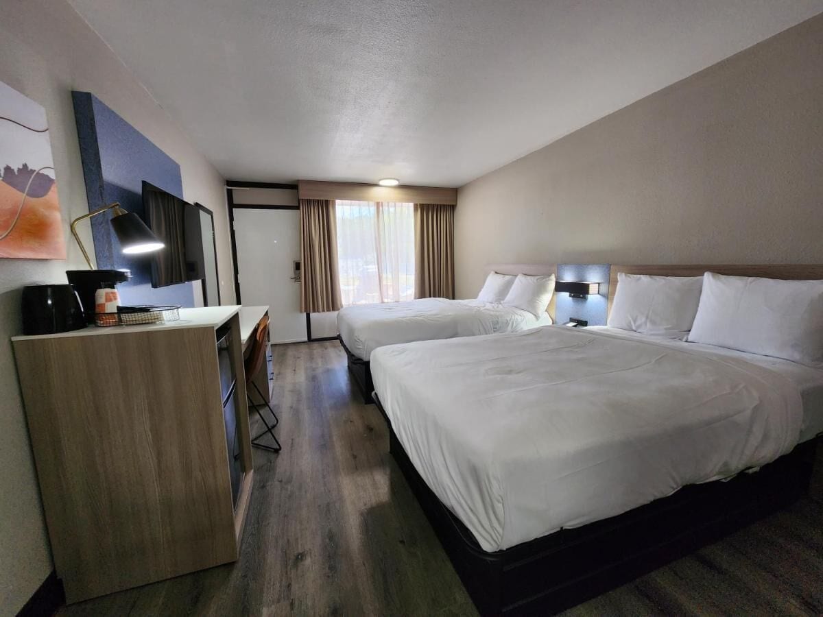A hotel room with two beds, a desk, a chair, a coffee maker, and a TV.