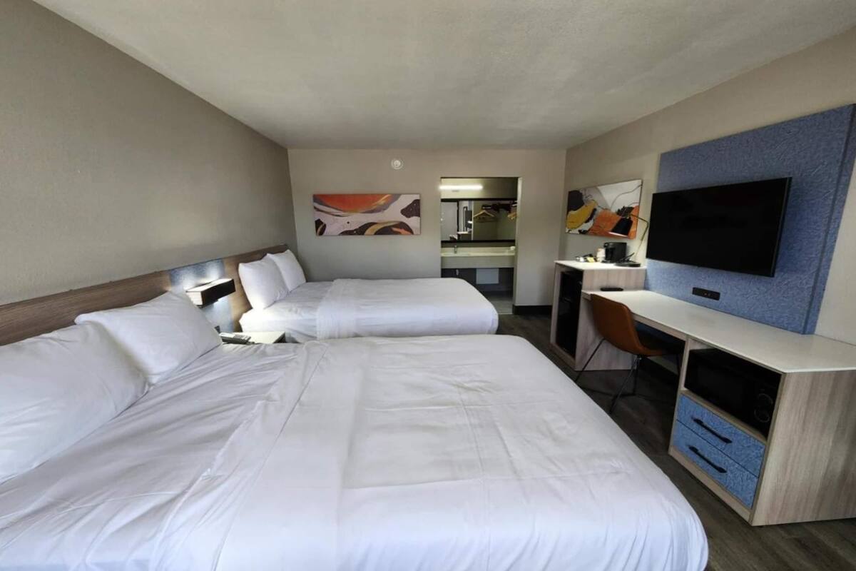 Habitación de hotel con dos camas, un escritorio, una silla, un televisor y obras de arte en las paredes.