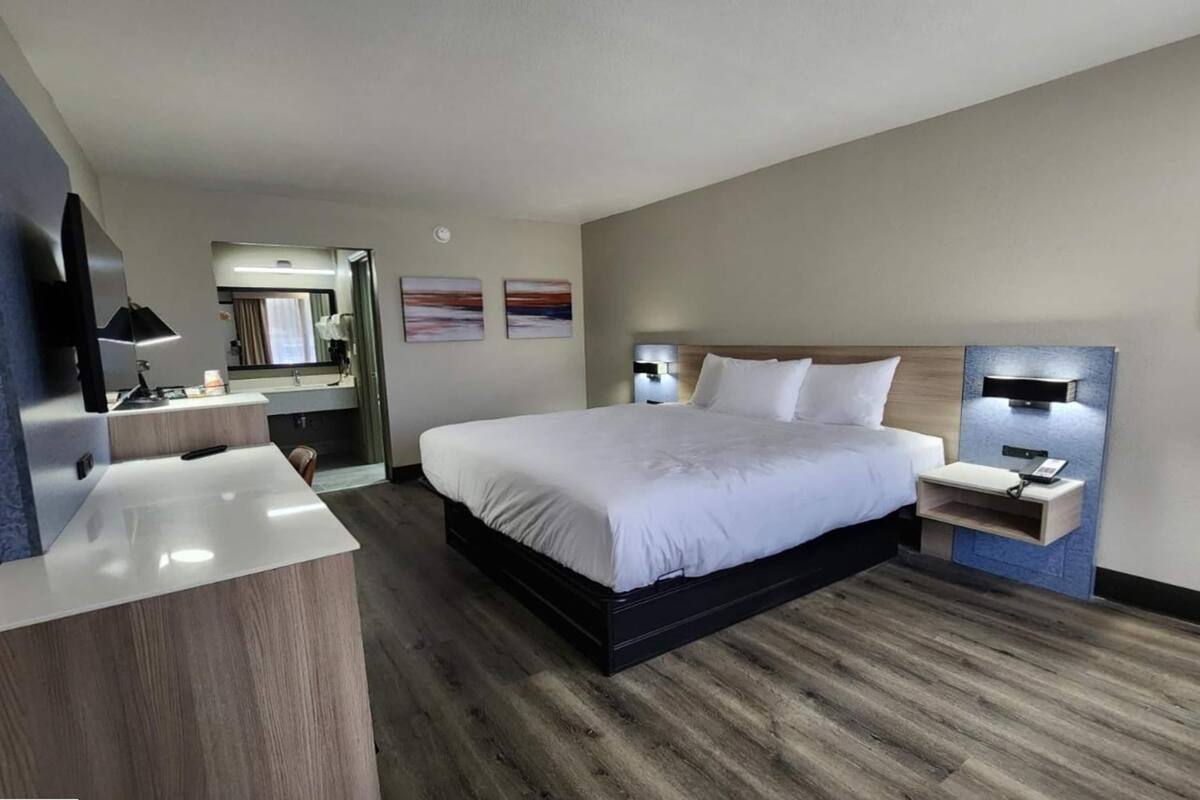 Una habitación de hotel moderna con una cama grande, un escritorio con una silla, una tocador con espejo y dos lámparas de pared.