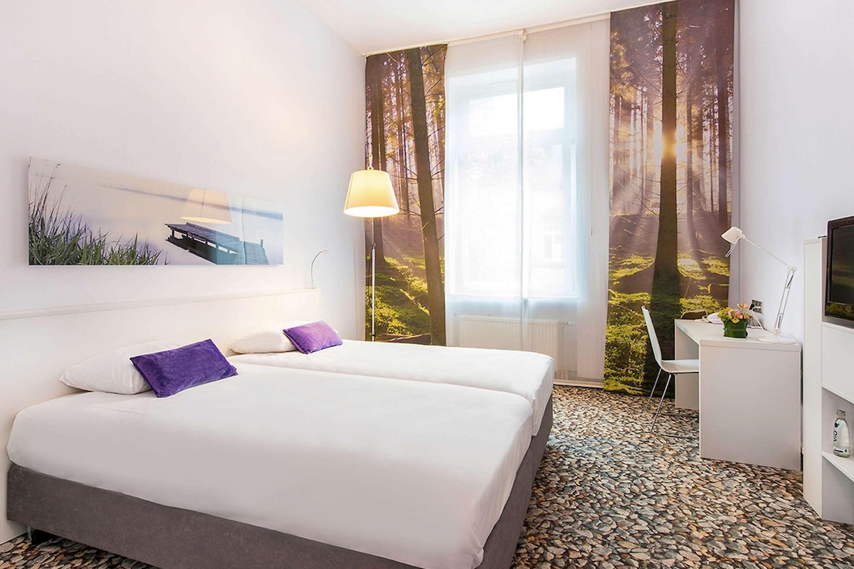 Een hotelkamer met een bed, een bureau, een stoel, een televisie en een raam met gordijnen.