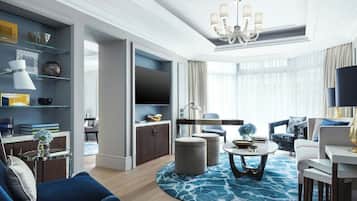 A modern living room with a chandelier, a flat-screen TV, and a blue patterned rug.