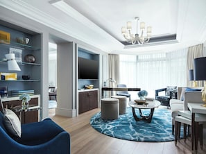 A modern living room with a chandelier, a flat-screen TV, and a blue patterned rug. - The Langham, Hong Kong (Kowloon)