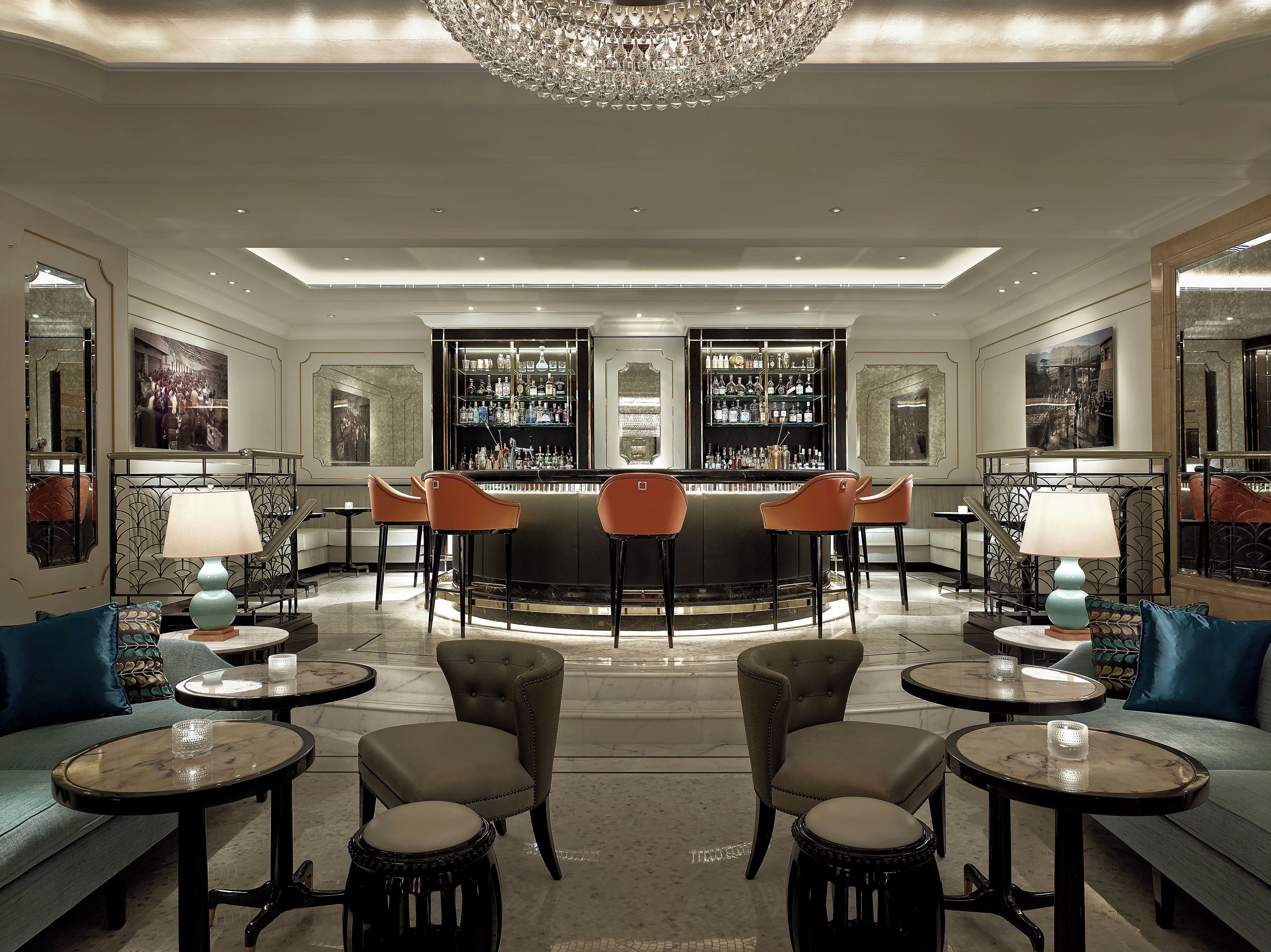 A bar area with a chandelier, bar stools, and a bar stocked with bottles.