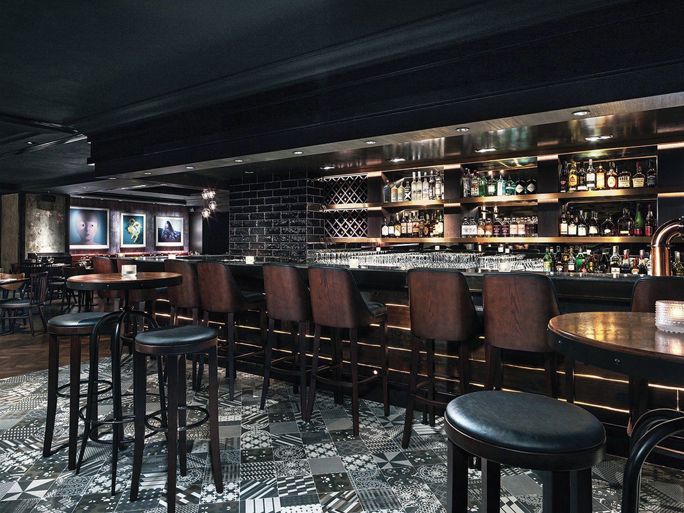 A bar area with multiple seating options, including bar stools and tables, and a variety of liquor bottles on shelves.