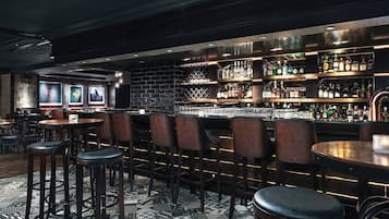 A bar area with multiple seating options, including bar stools and tables, and a variety of liquor bottles on shelves.